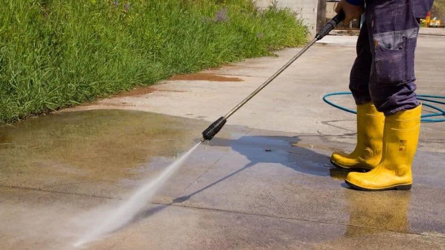 homem com botas de borracha lavando chão com uma lavadora de alta pressão